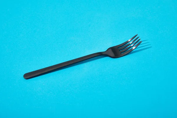 Metal shiny black fork on blue background — Stock Photo