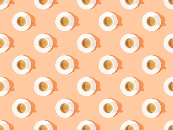 Ansicht von Tassen mit frischem Kaffee auf Tellern auf orangefarbenem, nahtlosem Hintergrundmuster — Stockfoto