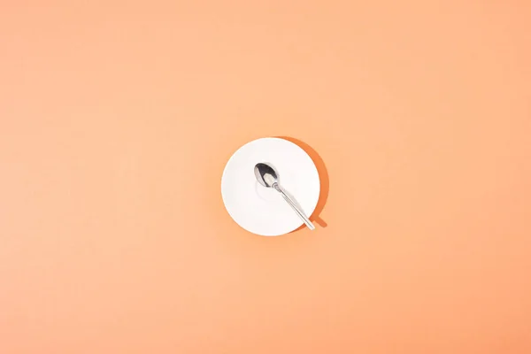 Top view of metal spoon on white round plate on orange background — Stock Photo