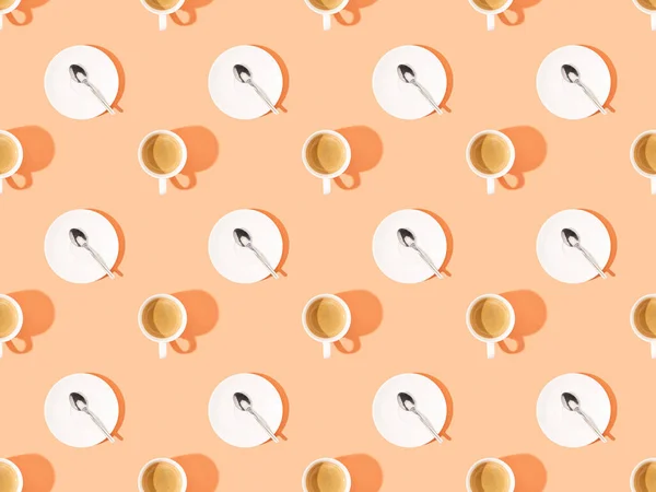 Vue de dessus des tasses de café frais et des cuillères sur des assiettes sur orange, motif de fond sans couture — Photo de stock