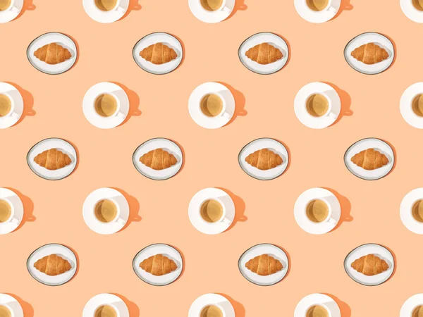 Top view of fresh croissants on plates and coffee on orange, seamless background pattern — Stock Photo