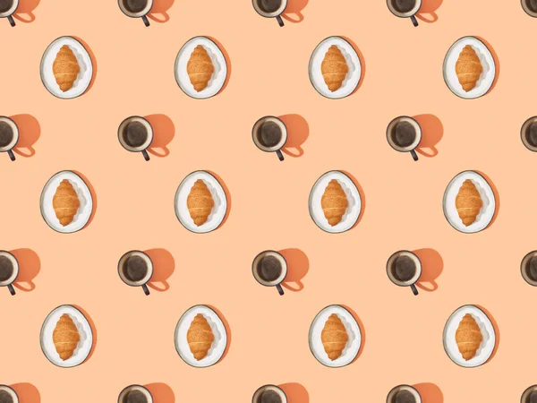Draufsicht auf frische Croissants auf Tellern und Kaffee auf orangefarbenem, nahtlosem Hintergrundmuster — Stockfoto