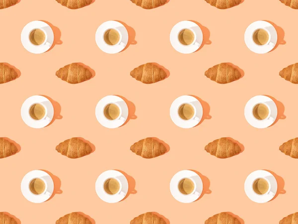 Top view of fresh croissants on plates and coffee on orange, seamless background pattern — Stock Photo