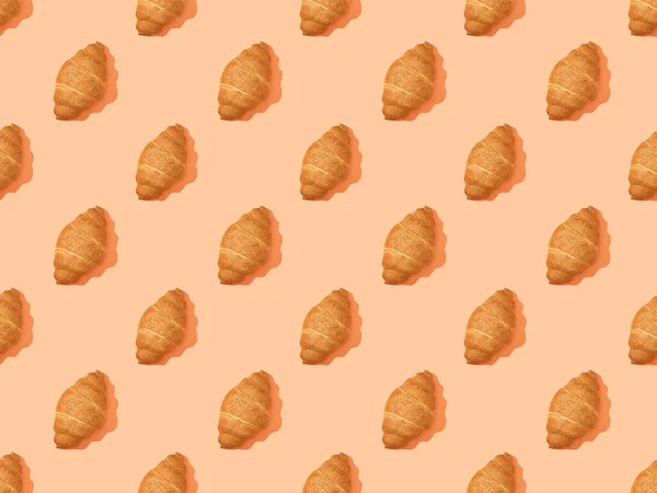 Draufsicht auf frische Croissants auf orangefarbenem, nahtlosem Hintergrundmuster — Stockfoto
