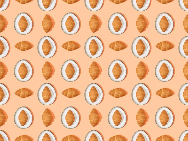 Draufsicht auf frische Croissants auf Tellern auf orangefarbenem, nahtlosem Hintergrundmuster — Stockfoto