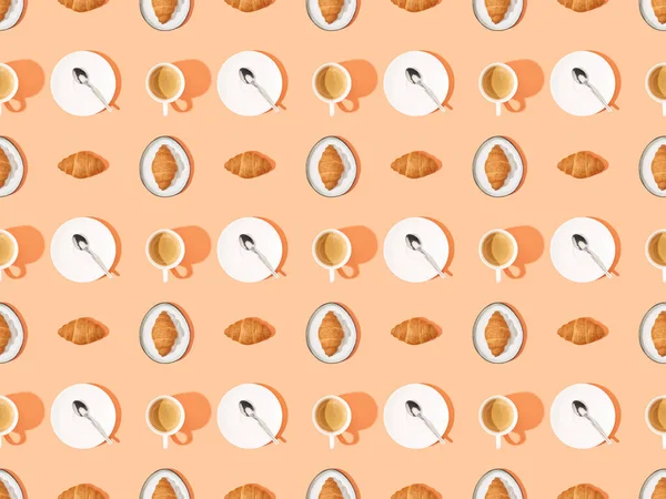 Top view of spoons, fresh croissants on plates and coffee on orange, seamless background pattern — Stock Photo