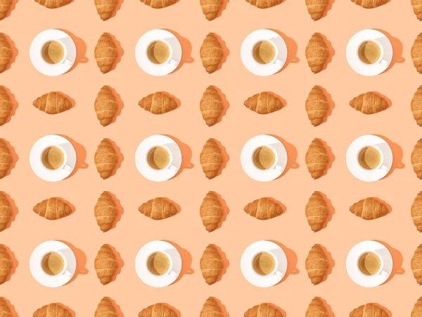 Top view of fresh croissants on plates and coffee on orange, seamless background pattern — Stock Photo