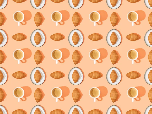 Top view of fresh croissants on plates and coffee on orange, seamless background pattern — Stock Photo