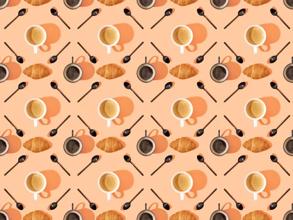 Vista superior de las tazas de café fresco, croissants y cucharas en naranja, patrón de fondo sin costuras - foto de stock