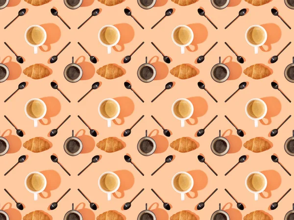 Top view of cups of fresh coffee, croissants and spoons on orange, seamless background pattern — Stock Photo