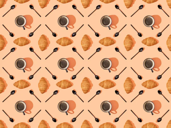 Top view of spoons, fresh croissants and coffee on orange, seamless background pattern — Stock Photo