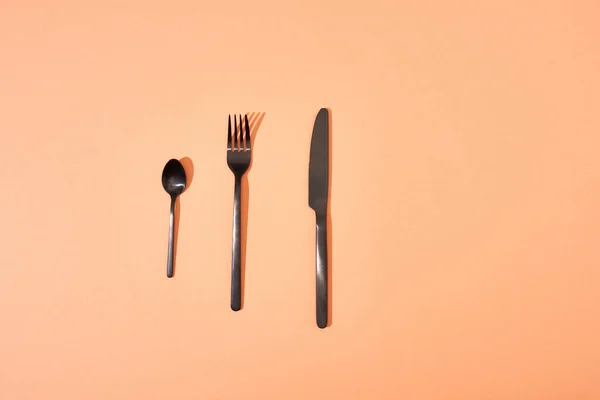 Top view of metal shiny black fork, spoon and knife on orange background — Stock Photo