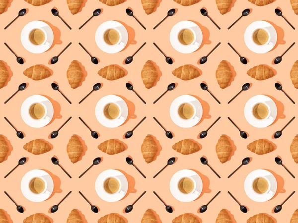 Vista superior de cucharas, cruasanes frescos en platos y café sobre naranja, patrón de fondo sin costuras - foto de stock