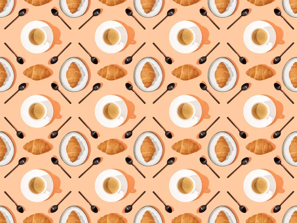 Top view of spoons, fresh croissants on plates and coffee on orange, seamless background pattern — Stock Photo