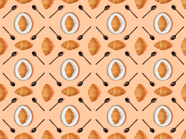 Top view of spoons and fresh croissants on plates on orange, seamless background pattern — Stock Photo