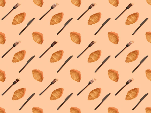 Top view of cutlery and fresh croissants on orange, seamless background pattern — Stock Photo