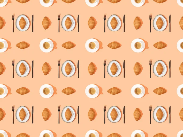 Top view of cutlery, fresh croissants on plates and coffee on orange, seamless background pattern — Stock Photo