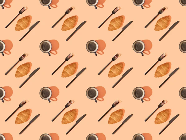 Vista superior de cubiertos, cruasanes frescos y café sobre naranja, patrón de fondo sin costuras — Stock Photo