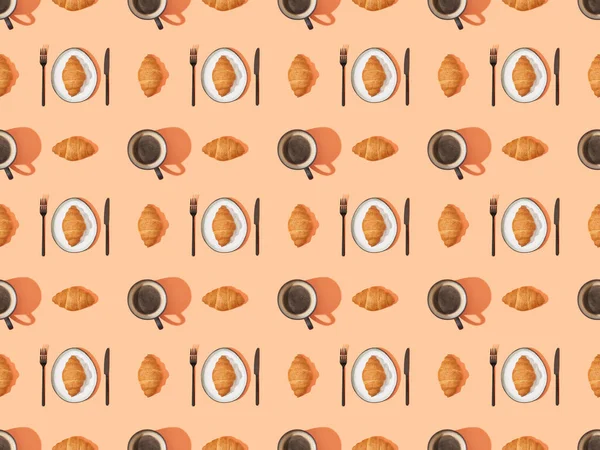 Top view of cutlery, fresh croissants and coffee on orange, seamless background pattern — Stock Photo