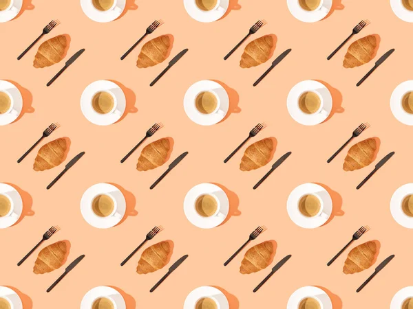 Ansicht von Besteck, frischen Croissants auf Tellern und Kaffee auf orangefarbenem, nahtlosem Hintergrundmuster — Stockfoto