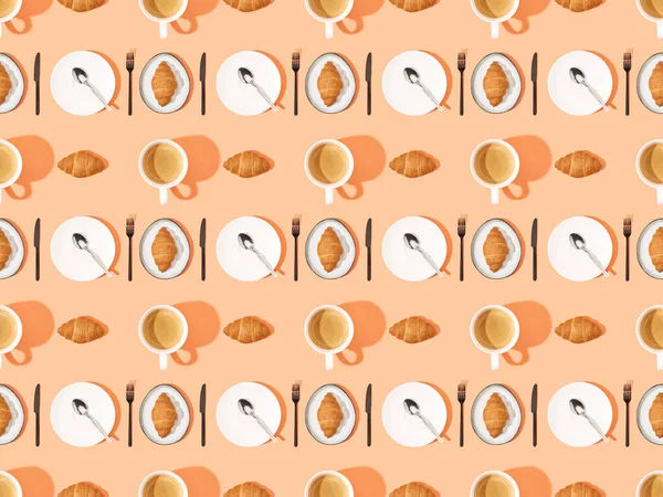 Top view of cutlery, fresh croissants on plates and coffee on orange, seamless background pattern — Stock Photo