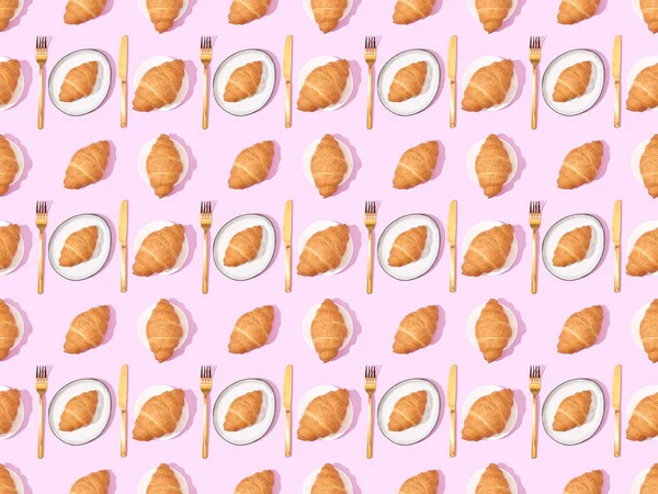 Ansicht von Besteck und Croissants auf Tellern auf rosa, nahtlosem Hintergrundmuster — Stockfoto