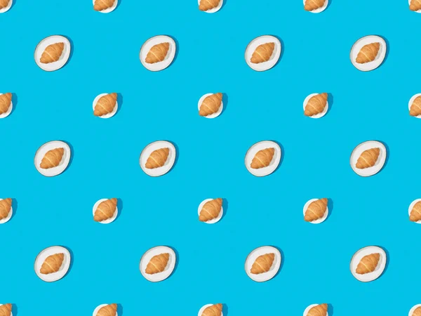 Draufsicht auf frische Croissants auf Tellern auf blauem, nahtlosem Hintergrundmuster — Stockfoto