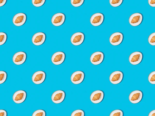 Top view of fresh croissants on plates on blue, seamless background pattern — Stock Photo