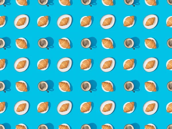 Top view of croissants on plates and coffee on blue, seamless background pattern — Stock Photo