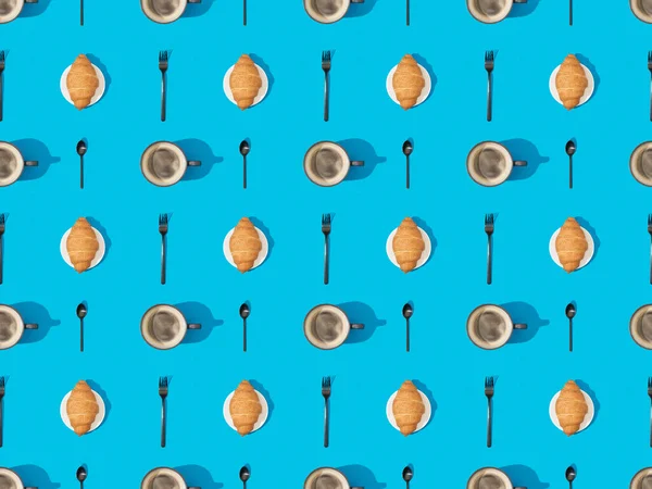 Top view of cutlery, croissants on plates and coffee on blue, seamless background pattern — Stock Photo