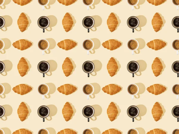 Draufsicht auf Croissants und Kaffee auf beigem, nahtlosem Hintergrundmuster — Stockfoto