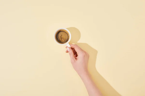 Cropped view of woman holding cup of fresh coffee on beige background — Stock Photo