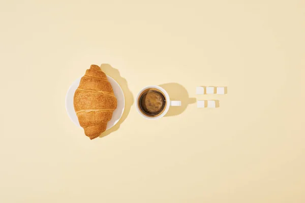 Draufsicht auf Croissant, Klumpen Zucker und Kaffee auf beigem Hintergrund — Stockfoto
