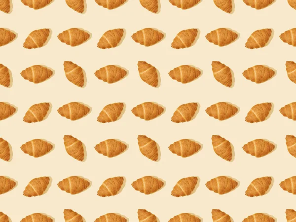 Draufsicht auf frische Croissants auf beigem, nahtlosem Hintergrundmuster — Stockfoto