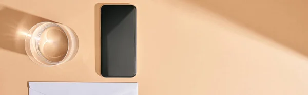 Plano panorámico de smartphone, vaso de agua y sobre fondo beige - foto de stock