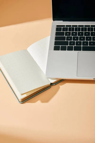 Vista de ángulo alto del cuaderno en blanco abierto y el ordenador portátil sobre fondo beige - foto de stock