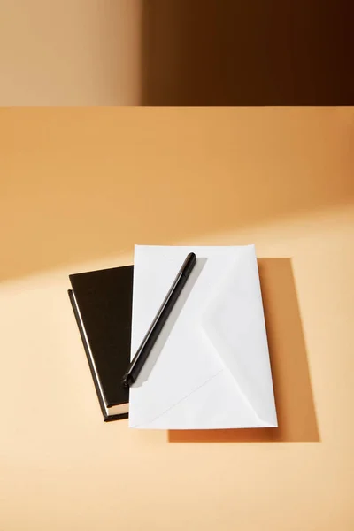 Envelope, caneta e caderno preto na superfície bege — Fotografia de Stock