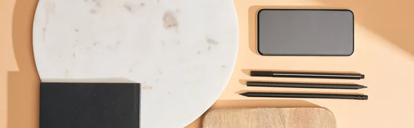 Panoramic shot of wooden and marble boards, smartphone, notebook and pens on beige background — Stock Photo