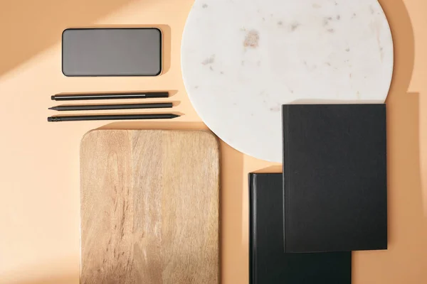 Vista superior de placas de madeira e mármore, smartphone, notebooks e canetas em fundo bege — Fotografia de Stock