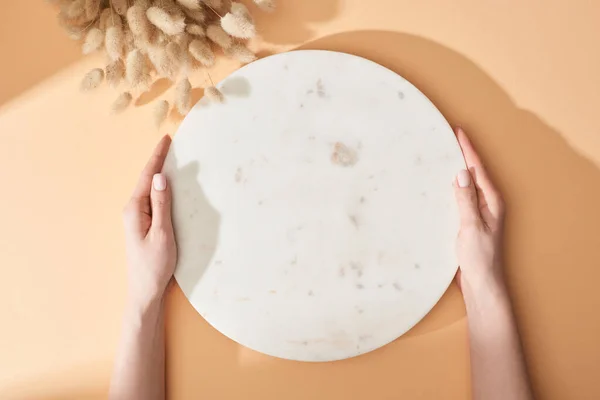 Vue partielle de la femme tenant le panneau de marbre près des épillets lagurus sur fond beige — Photo de stock