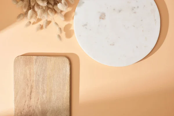 Top view of marble and wooden boards near lagurus spikelets on beige background — Stock Photo