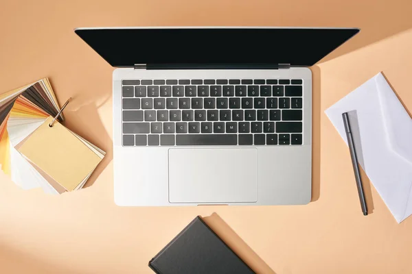 Ansicht von Laptop in der Nähe von Farbmustern, Notizbuch, Umschlag und Stift auf beigem Hintergrund — Stockfoto