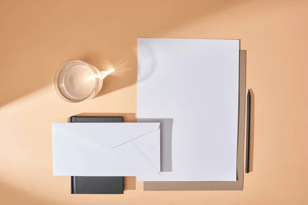 Top view of sheets of paper, envelope, pen, glass of water and notebook on beige background — Stock Photo