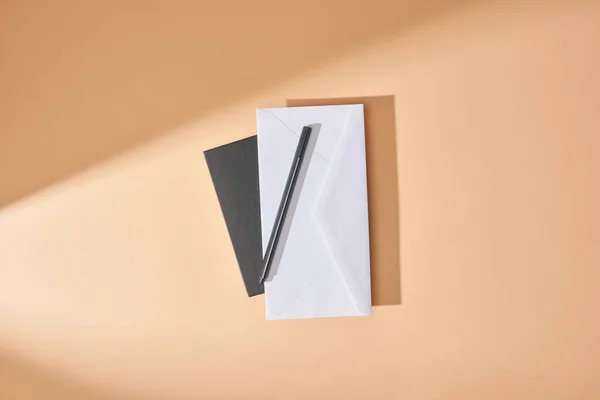 Top view of envelope and pen on notebook on beige background — Stock Photo