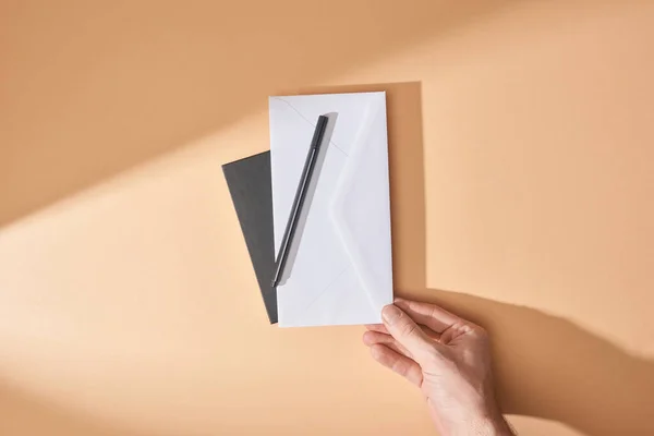 Vista parcial del hombre sosteniendo sobre y pluma cerca del cuaderno sobre fondo beige - foto de stock