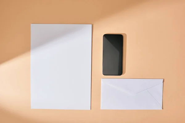 Top view of sheet of paper, smartphone and envelope on beige background — Stock Photo