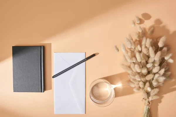 Top view of notebook, envelope, pen, glass of water and lagurus spikelets on beige background — Stock Photo