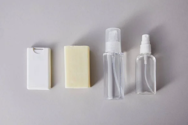 Pose plate avec désinfectant pour les mains dans des flacons de pulvérisation et savon antibactérien sur fond gris — Photo de stock