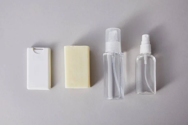 Tendido plano con desinfectante de manos en botellas de spray y jabón antibacteriano sobre fondo gris - foto de stock
