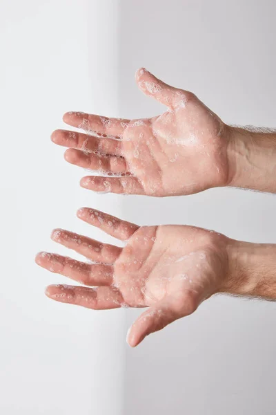 Partial view of man showing hands with soap foam on grey background background — Stock Photo